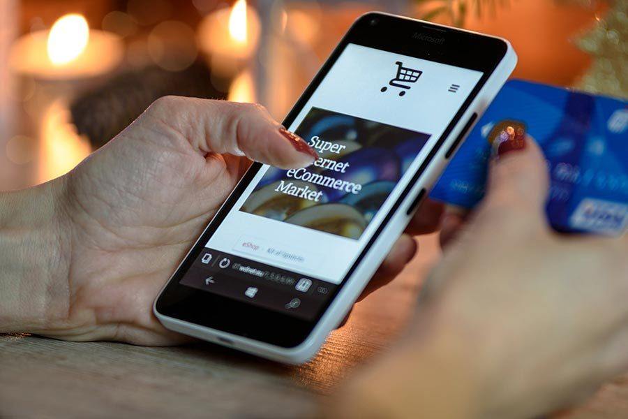 Person holding a smartphone with an e-commerce website on the screen, credit card in hand, indicating online shopping.