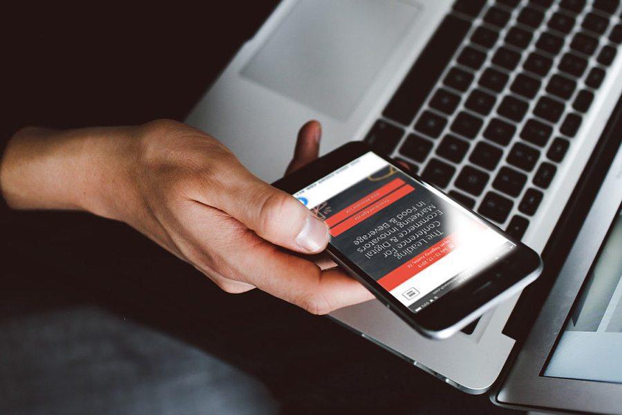 Person holding a smartphone with notification alerts on the screen, next to an open laptop.