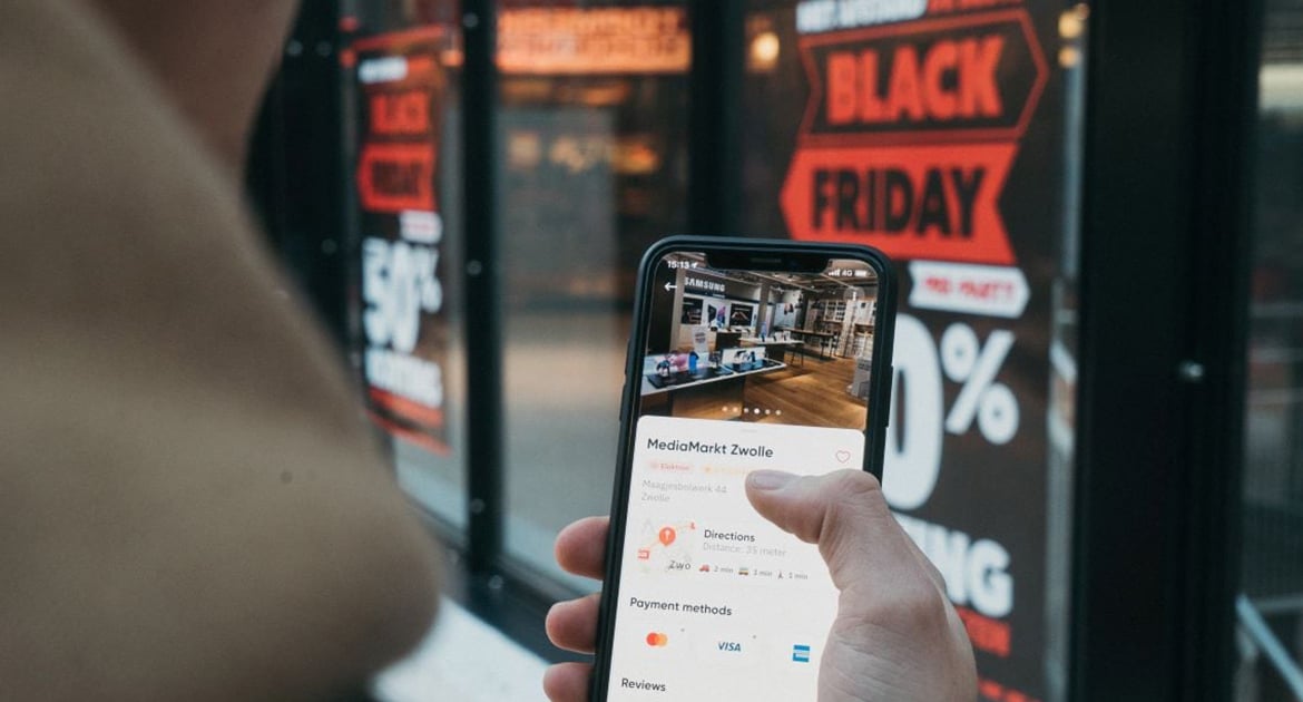 Person checking a Cyber Monday sale on a smartphone in front of a store with promotional signs.