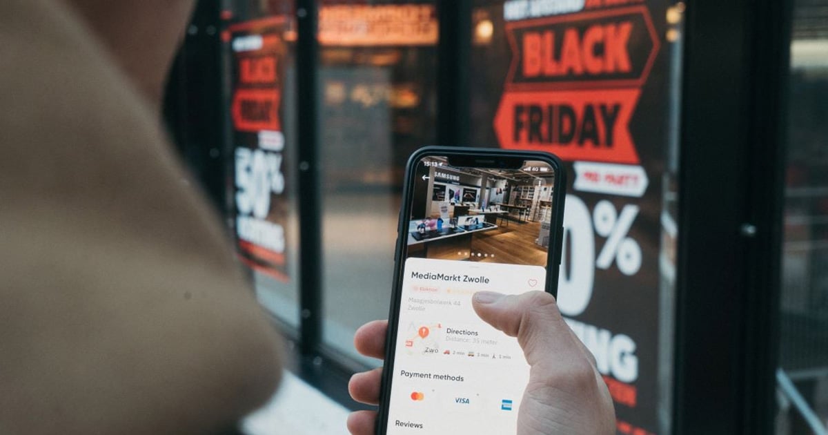 Person checking a Cyber Monday sale on a smartphone in front of a store with promotional signs.