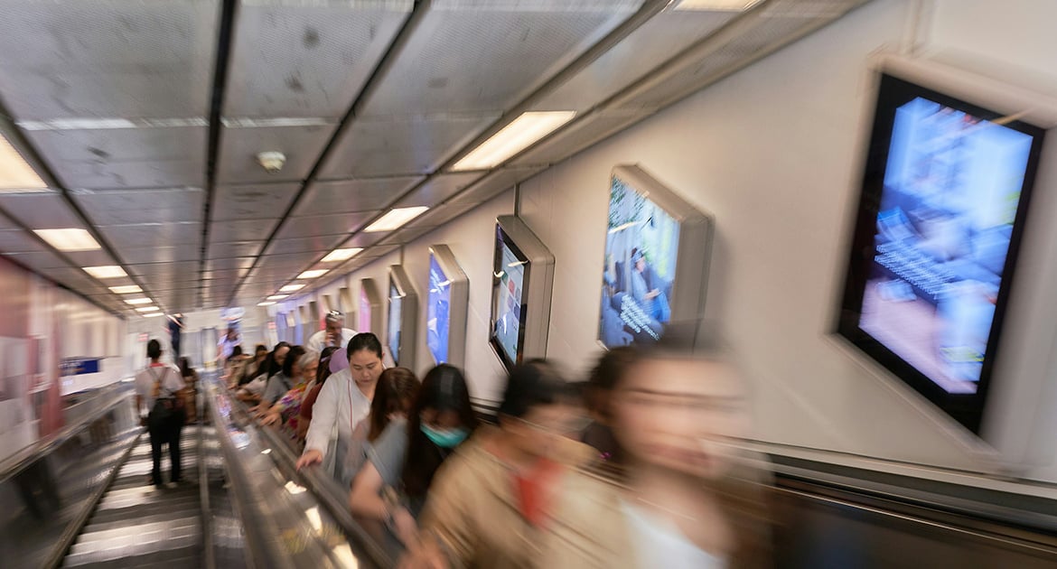 Commuters on a moving walkway passing by blurred PPC ads in a busy transit corridor.