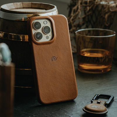 A Bullstrap Creative leather smartphone case on a table next to a glass of whiskey and a keyring.