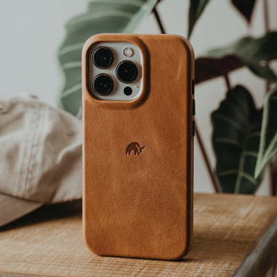 A smartphone encased in a Bullstrap brown leather case rests on a wooden surface.